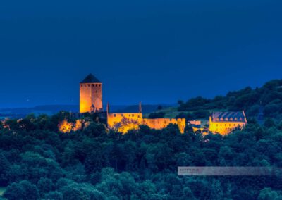 Blaue Stunde an der beleuchteten Burg Lichtenberg. Dunkle Bäume und dunkler Nachthimmel umgeben die Burg