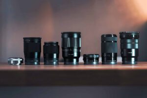 Beste Objektive Sony A7-Serie — Sigma und Sony Festbrennweiten und Zooms nebeneinander auf Holztisch
